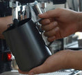Black stainless steel milk frothing jug with ergonomic handle for home espresso machines