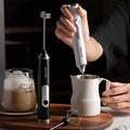 Compact USB rechargeable milk frother with stainless steel whisk and replaceable brush heads in black and white
